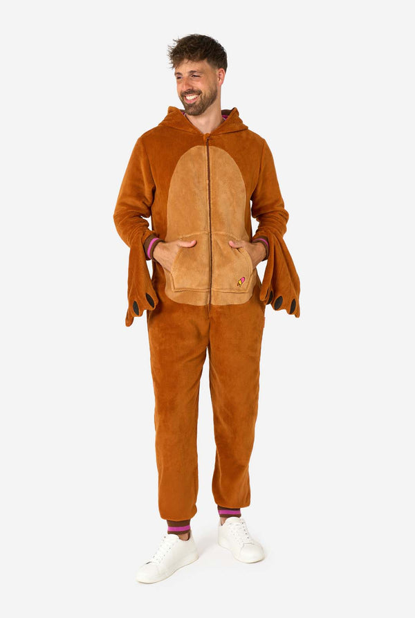 Ein fröhlicher Mann trägt einen braunen Erwachsenen-Onesie in Walross-Optik. Der Onesie hat eine Kapuze mit Reißzähnen, aufgenähte Handschuhe in Pfotenform und verspielte Walross-Details – perfekt für gemütliches Faulenzen oder Kostümpartys. Ganzkörperbild und der Mann hält seine Hände in den Taschen.