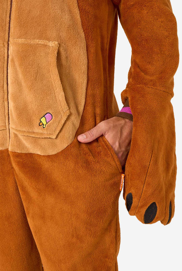Ein fröhlicher Mann trägt einen braunen Erwachsenen-Onesie in Walross-Optik. Der Onesie hat eine Kapuze mit Reißzähnen, aufgenähte Handschuhe in Pfotenform und verspielte Walross-Details – perfekt für gemütliches Faulenzen oder Kostümpartys. Nahaufnahme der Tasche.