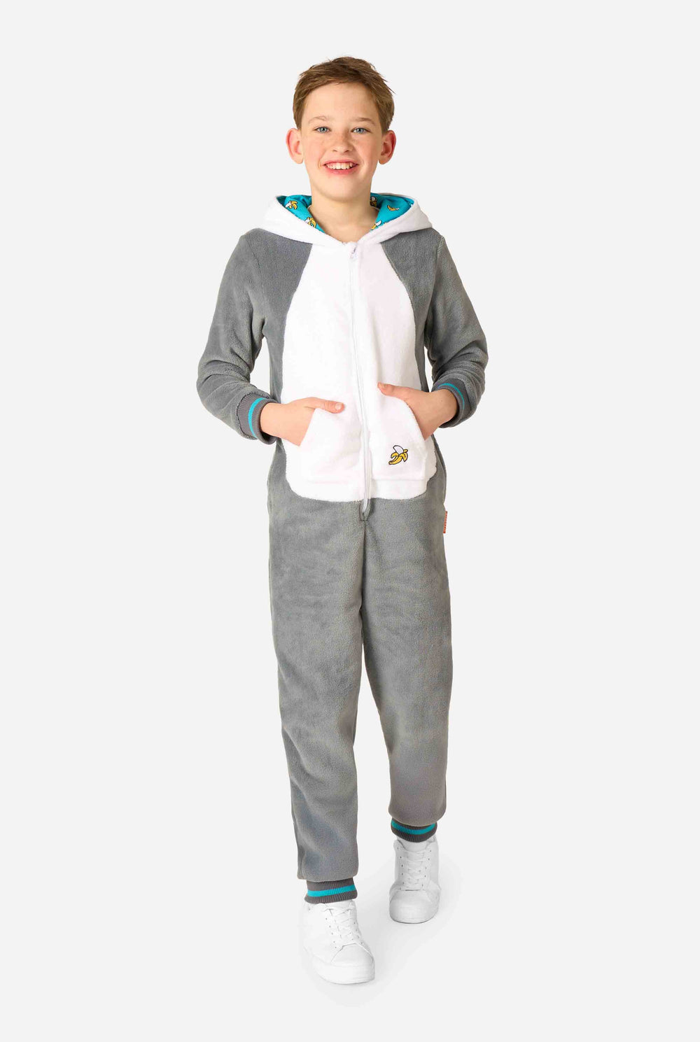 Kind trägt einen gemütlichen, unisex Kinder-Onesie im Lemur-Design aus grau-weißem Plüschstoff. Die Kapuze zeigt ein Cartoon-Lemurgesicht mit Ohren, und auf der Tasche befindet sich ein verspielter Bananenaufdruck.