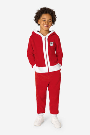 Ganzkörperansicht eines Kindes, das in einem roten Santa-Onesie mit weißer Einfassung und weißen Sneakers steht und lächelt.