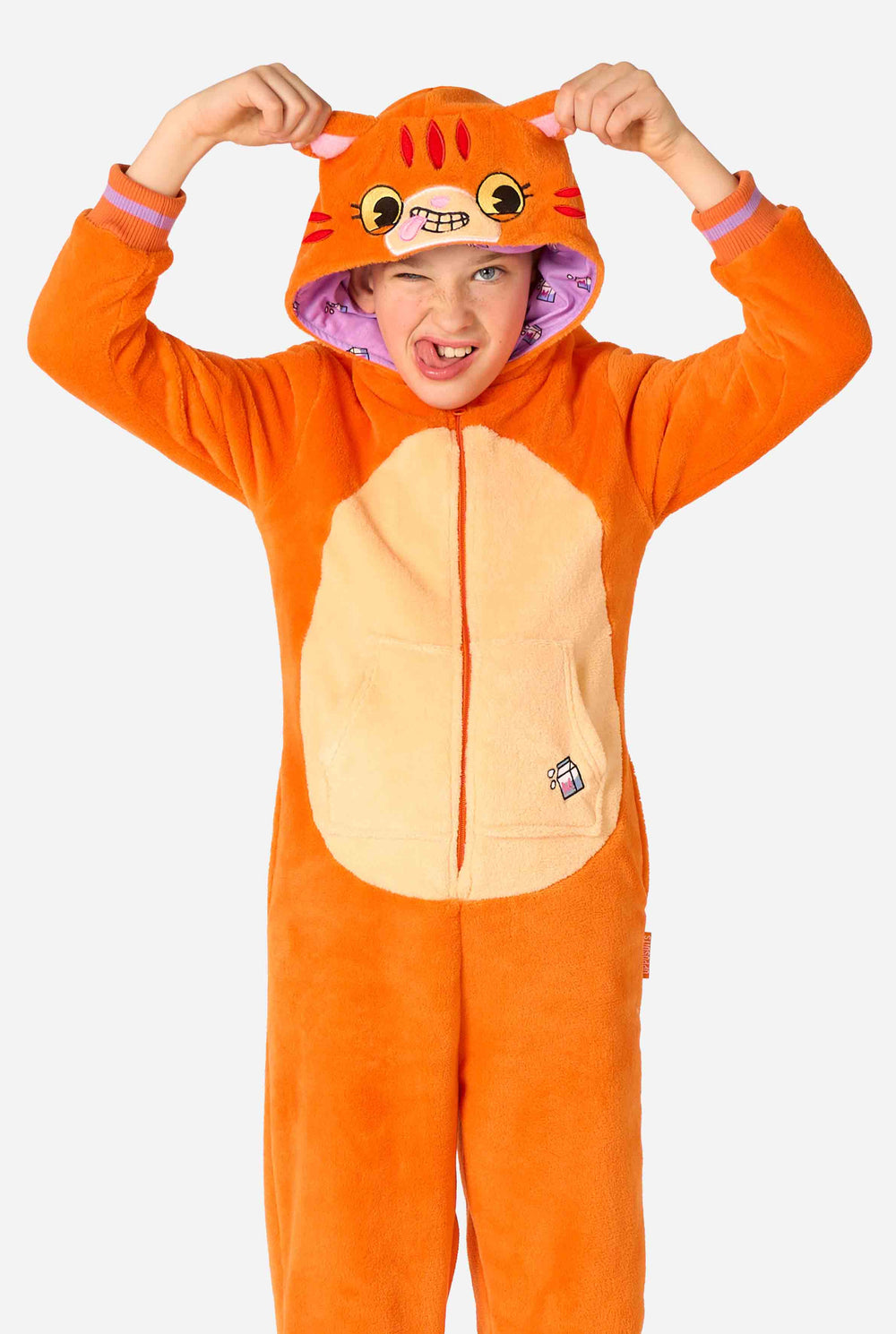 Kind trägt einen verspielten, unisex Kinder-Onesie im Design einer rot-orangefarbenen Katze, mit Kapuze, die ein Cartoon-Katzengesicht und Ohren zeigt, sowie einem hellbeigen Bauchpaneel. Das Kind zieht eine lustige Grimasse vor einem schlichten Hintergrund.
