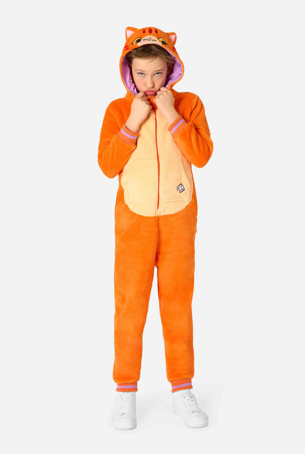 Kind trägt einen verspielten, unisex Kinder-Onesie im Design einer rot-orangefarbenen Katze, mit Kapuze, die ein Cartoon-Katzengesicht und Ohren zeigt, sowie einem hellbeigen Bauchpaneel. Das Kind zieht eine lustige Grimasse vor einem schlichten Hintergrund. Ganzkörperaufnahme.