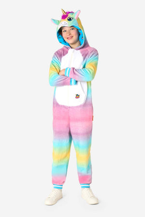 Ein lächelndes Kind trägt einen weißen, rosa, blauen und gelben Kinderstrampler, der als Einhorn gestaltet ist. Der Einhorn-Einteiler verfügt über eine Kapuze, die einem Einhornkopf ähnelt, und weitere verspielte Details. Ganzkörperbild.