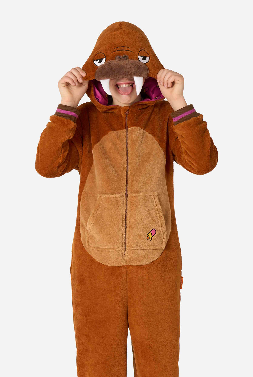 Ein fröhliches Kind trägt einen braunen Kinder-Onesie in Walross-Optik. Der Onesie hat eine Kapuze mit Reißzähnen, aufgenähte Handschuhe in Pfotenform und verspielte Walross-Details – perfekt für gemütliches Faulenzen oder Kostümpartys.
