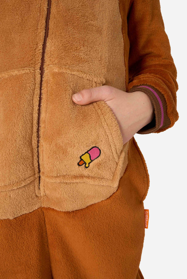 Ein fröhliches Kind trägt einen braunen Kinder-Onesie in Walross-Optik. Der Onesie hat eine Kapuze mit Reißzähnen, aufgenähte Handschuhe in Pfotenform und verspielte Walross-Details – perfekt für gemütliches Faulenzen oder Kostümpartys. Nahaufnahme.
