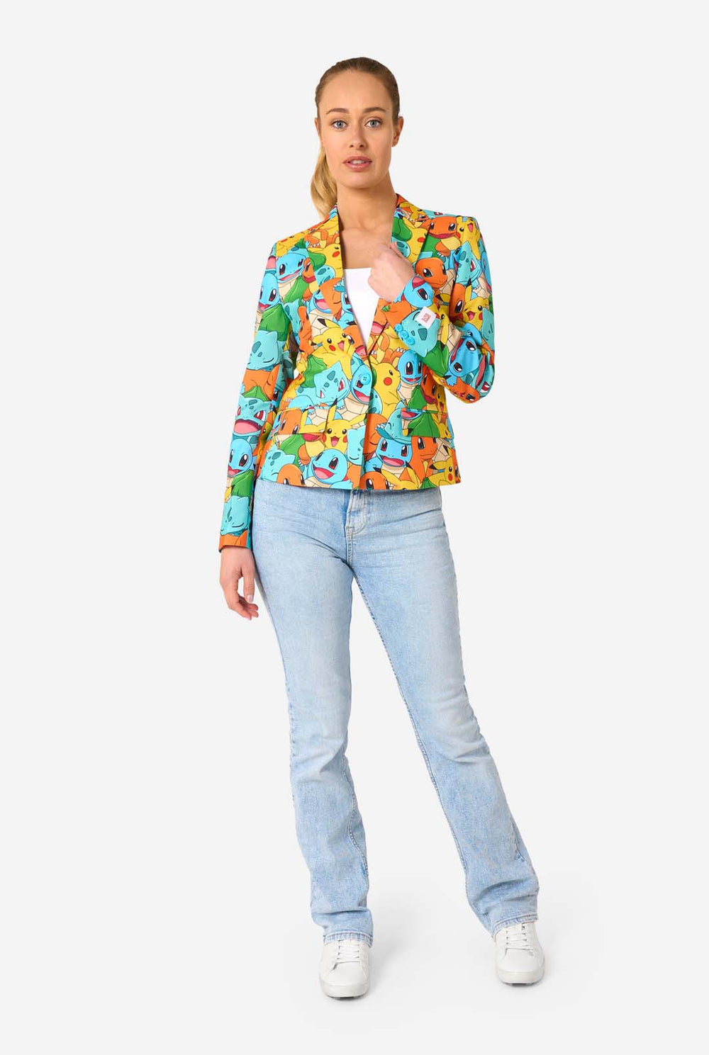 Eine Frau trägt einen mehrfarbigen Pokemon-Blazer, auf dem Figuren wie Pikachu, Squirtle, Charmander und Bulbasaur abgebildet sind. Sie hält die Jacke und lächelt in die Kamera.
