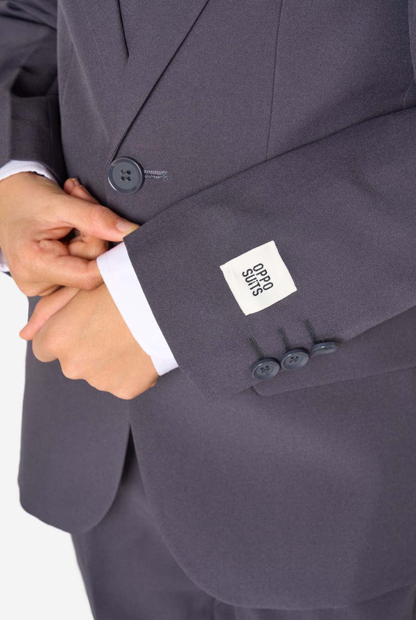 Junge in einem eleganten, anthrazitfarbenen Anzug mit weißem Hemd und selbstbewusstem Lächeln. Perfektes formelles Outfit für besondere Anlässe, Hochzeiten und Partys.