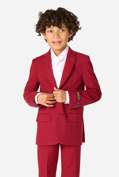 Kind trägt einen stilvollen bordeauxroten Anzug mit weißem Hemd, schaut selbstbewusst. Perfektes festliches Outfit für besondere Anlässe, Hochzeiten und Partys von Jungen.