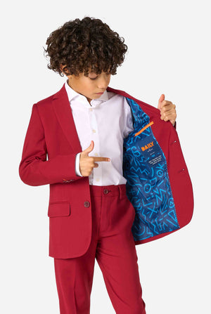 Kind trägt einen stilvollen bordeauxroten Anzug mit weißem Hemd, schaut selbstbewusst. Perfektes festliches Outfit für besondere Anlässe, Hochzeiten und Partys von Jungen. Hält eine Seite der Jacke geöffnet.