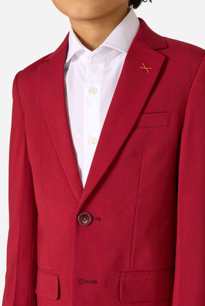 Kind trägt einen stilvollen bordeauxroten Anzug mit weißem Hemd, schaut selbstbewusst. Perfektes festliches Outfit für besondere Anlässe, Hochzeiten und Partys von Jungen. Nahaufnahme des Oberkörpers.