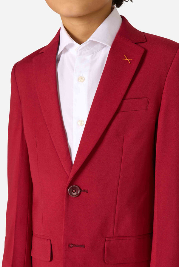 Kind trägt einen stilvollen bordeauxroten Anzug mit weißem Hemd, schaut selbstbewusst. Perfektes festliches Outfit für besondere Anlässe, Hochzeiten und Partys von Jungen. Nahaufnahme des Oberkörpers.