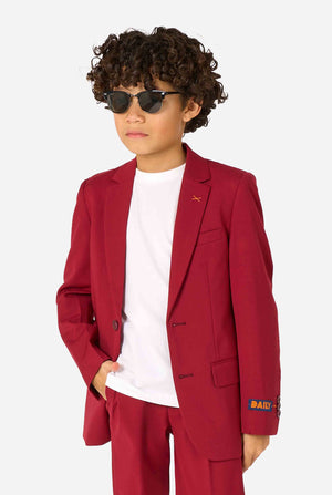 Kind trägt einen stilvollen bordeauxroten Anzug mit weißem Hemd, schaut selbstbewusst. Perfektes festliches Outfit für besondere Anlässe, Hochzeiten und Partys von Jungen.