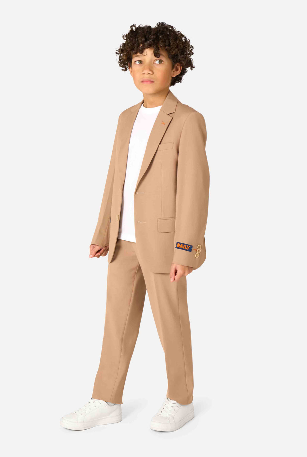 Kind trägt einen stilvollen hellbraunen/beigen Anzug mit weißem Hemd, schaut weg von der Kamera. Perfektes festliches Outfit für besondere Anlässe, Hochzeiten und Partys von Jungen.