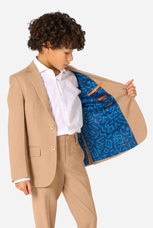 Kind trägt einen stilvollen hellbraunen/beigen Anzug mit weißem Hemd, schaut weg von der Kamera. Perfektes festliches Outfit für besondere Anlässe, Hochzeiten und Partys von Jungen. Hält eine Seite der Jacke geöffnet.