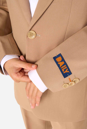 Kind trägt einen stilvollen hellbraunen/beigen Anzug mit weißem Hemd, schaut weg von der Kamera. Perfektes festliches Outfit für besondere Anlässe, Hochzeiten und Partys von Jungen. Fokus auf die Ärmel.
