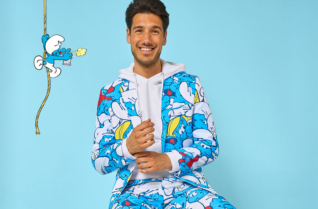 Das Bild zeigt einen hellblauen Hintergrund, links einen Schlümpf, der an einem Seil klettert, und einen Mann, der einen Herrenanzug mit einem kompletten Schlumpf-Motiv und einem weißen Hoodie trägt.
