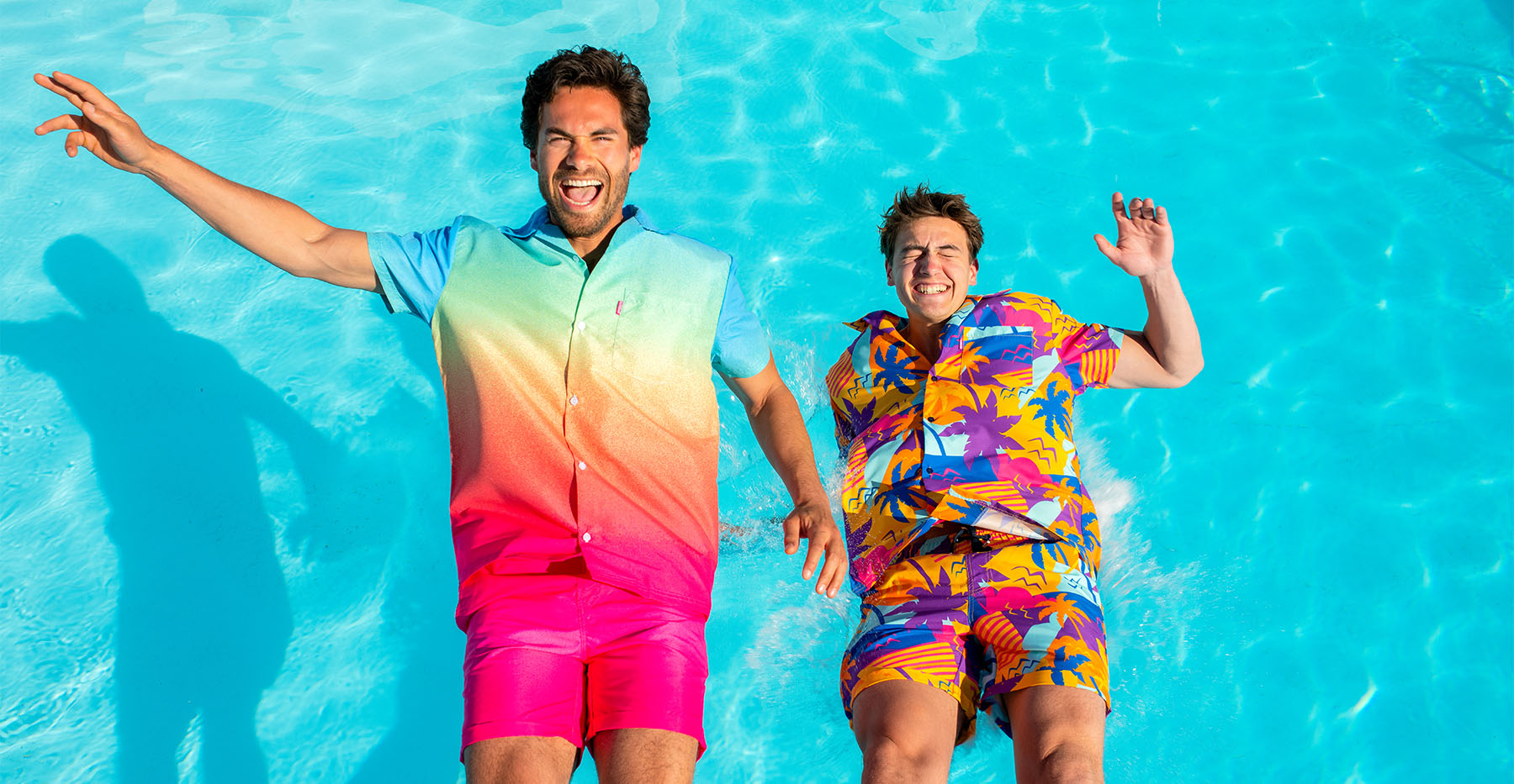 Two people in colorful swimwear standing in a pool with clear blue water.