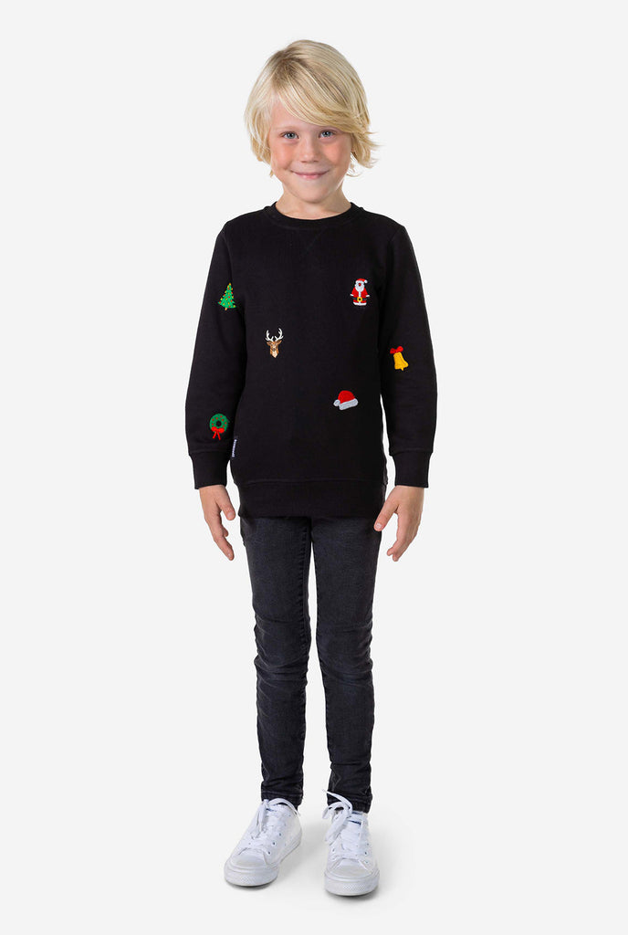 Kind trägt einen schwarzen Weihnachtspullover mit Weihnachtsikonen